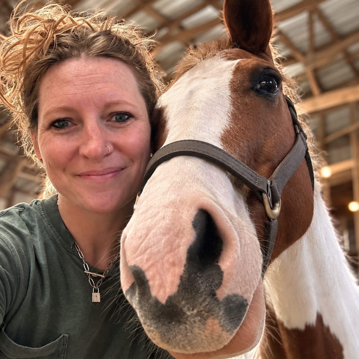 Holly Wright, founder of Cantr, cheek-to-cheek with her paint horse in a covered arena